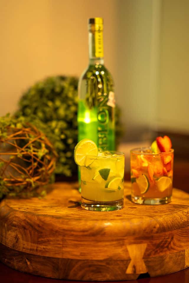 Two different flavored caipirinhas, strawberry and lime, surround by greenery decor.