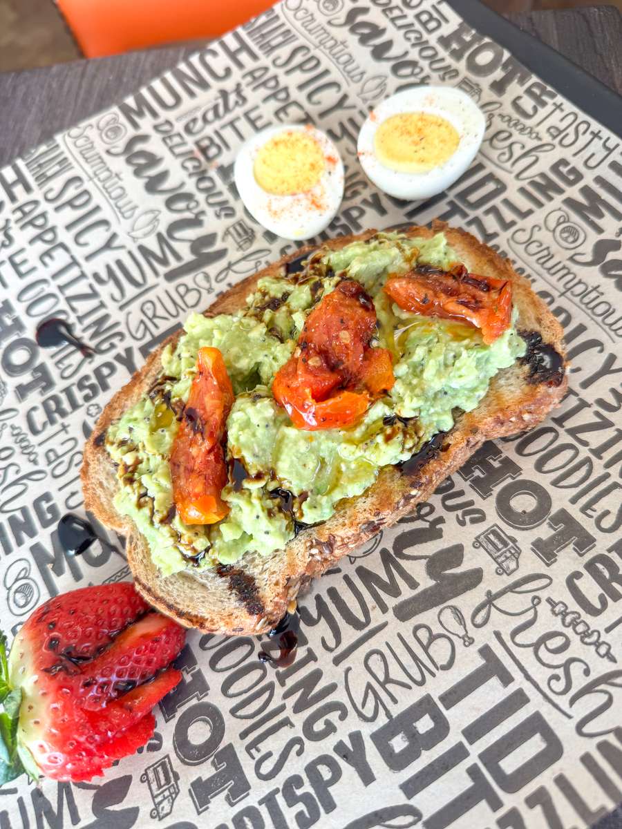 Everything Avocado Toast topped with tomato and a drizzle of balsamic vinegar on a multi-grain bread served with a boiled egg.