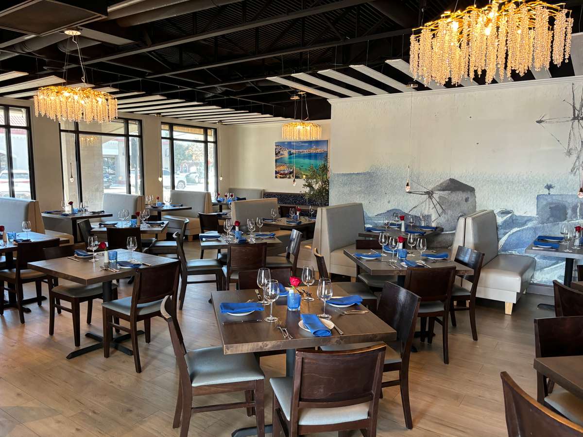 Upscale restaurant dining room with wooden tables, blue napkins, chandeliers, and coastal mural wall décor
