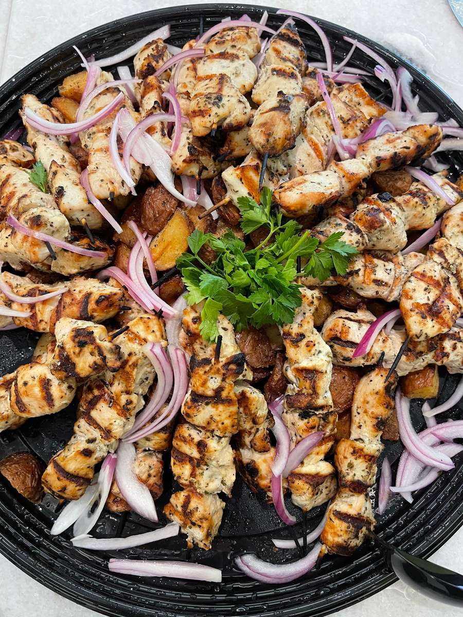 A large platter of grilled chicken skewers served over roasted potatoes, topped with sliced red onions and garnished with fresh parsley.