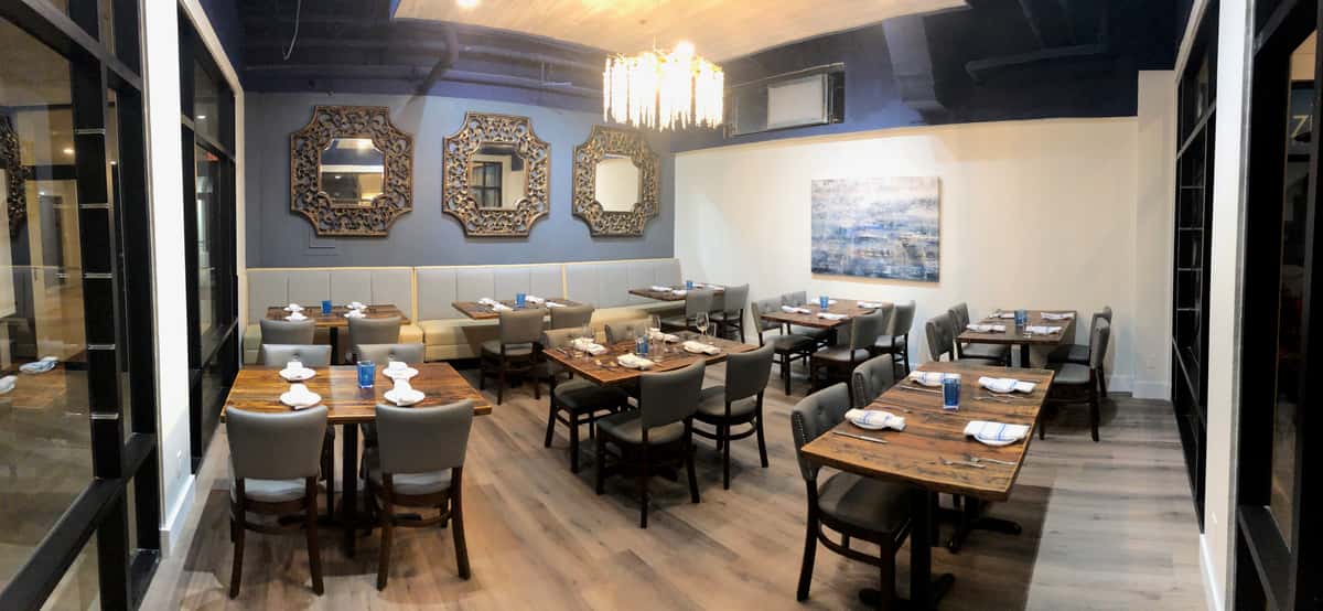 Modern restaurant dining room with wooden tables, upholstered chairs, chandelier lighting, and decorative mirrors on blue accent wall