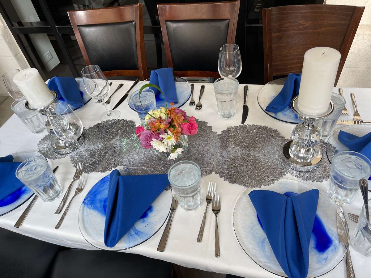Elegant table setting with blue napkins, glassware, candles, and floral centerpiece on white tablecloth