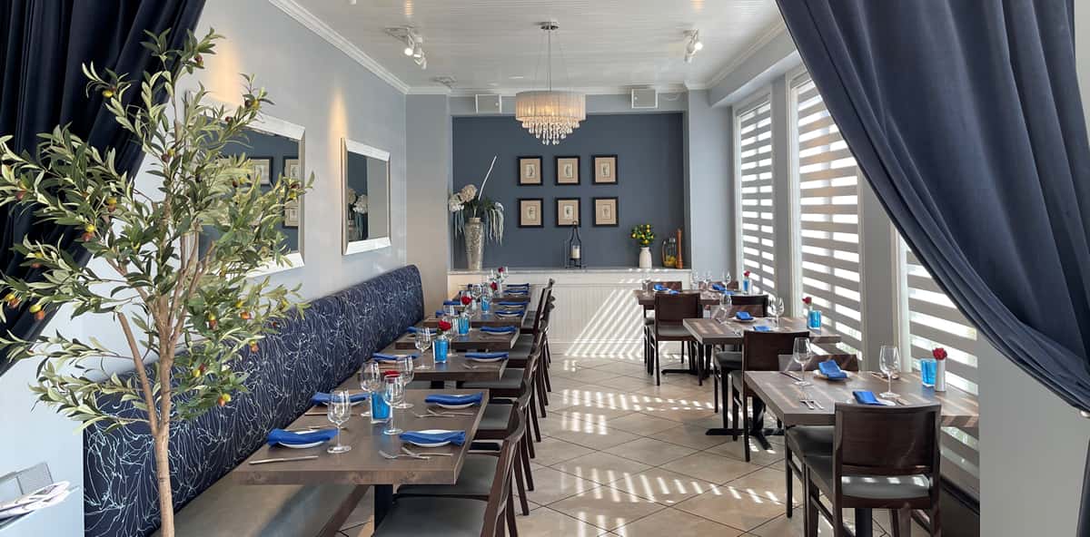 Bright, elegant dining room with blue accents, chandelier lighting, and neatly set wooden tables by large windows