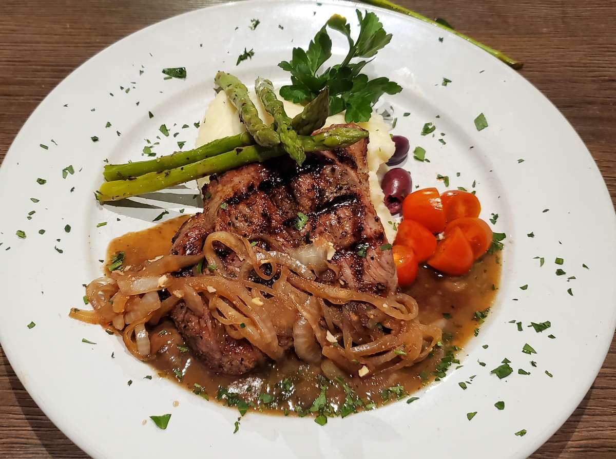 Grilled steak topped with caramelized onions and brown sauce, served with mashed potatoes, asparagus, and cherry tomatoes