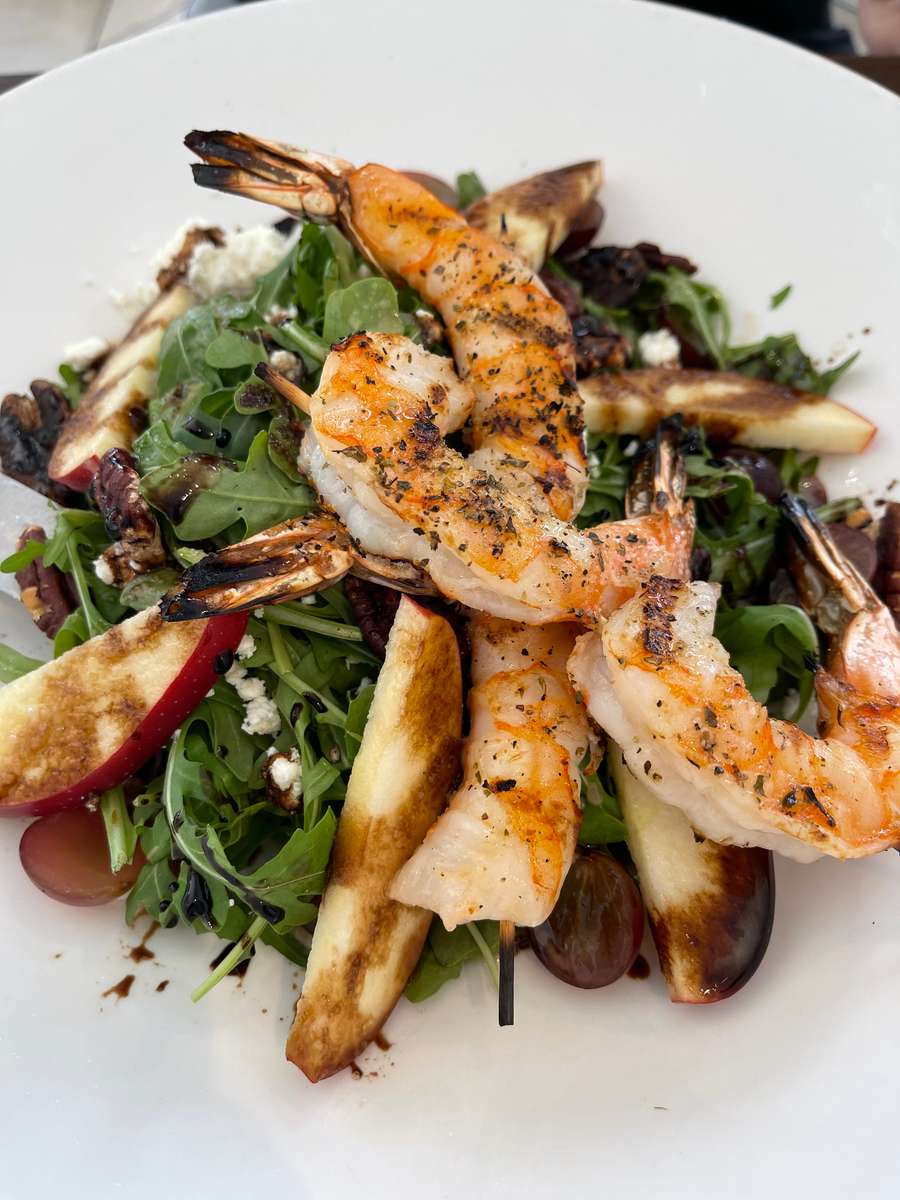 Grilled shrimp skewers over arugula salad with pears, grapes, feta, and balsamic drizzle on a white plate