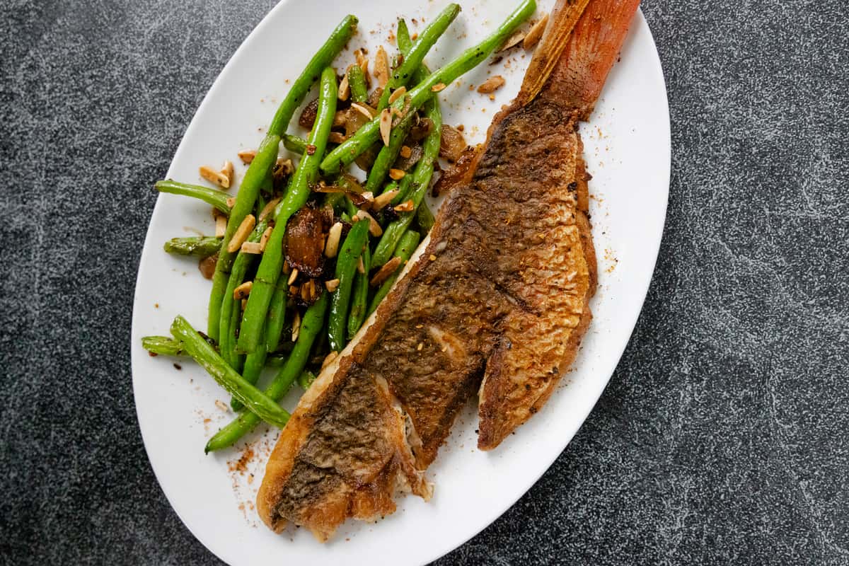Crispy whole fish fillet and bright green beans with toasted almonds served on a white plate at Jonathan the rub restaurant.