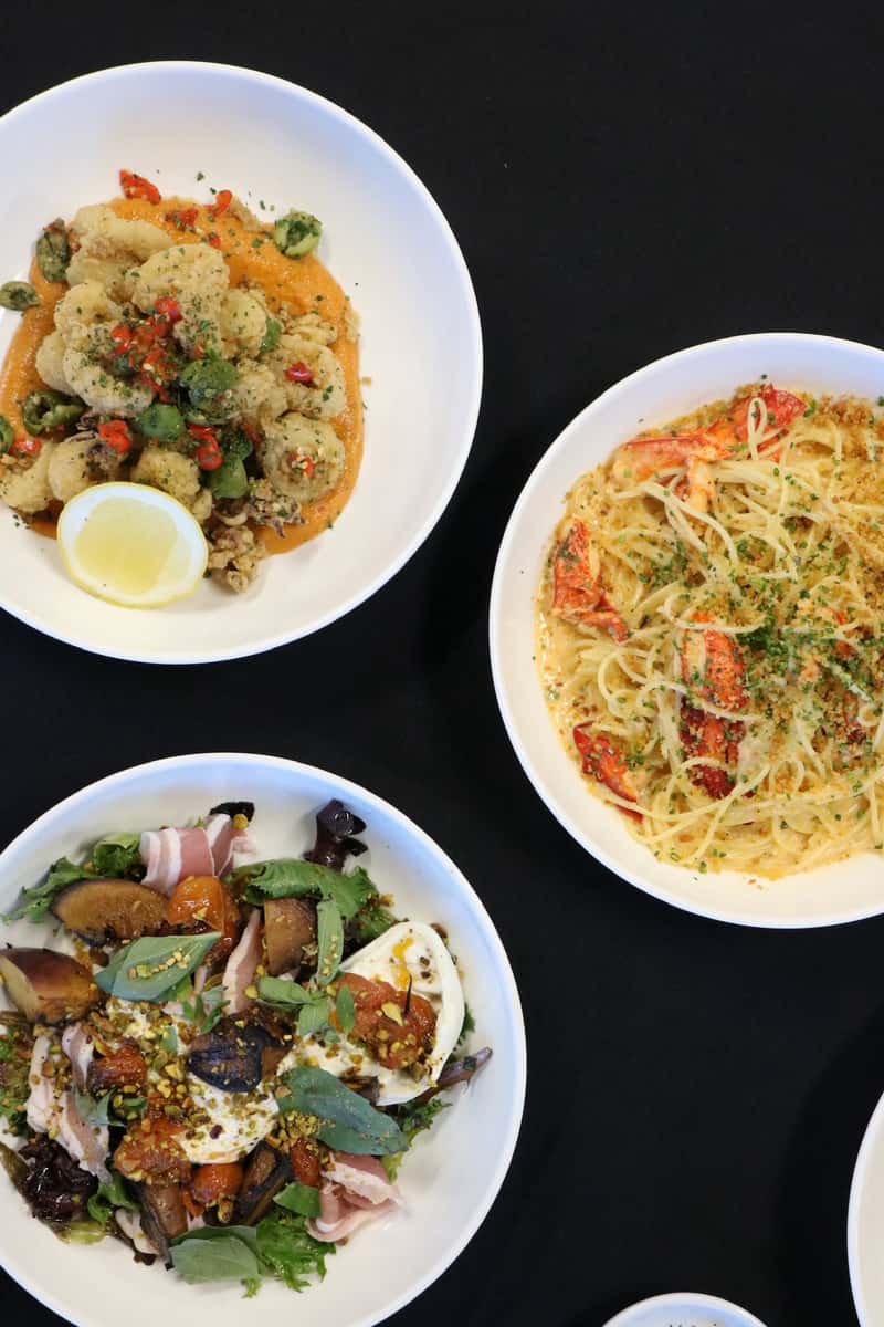 Assorted restaurant dishes including fried calamari, lobster pasta, and a fresh salad with prosciutto and burrata