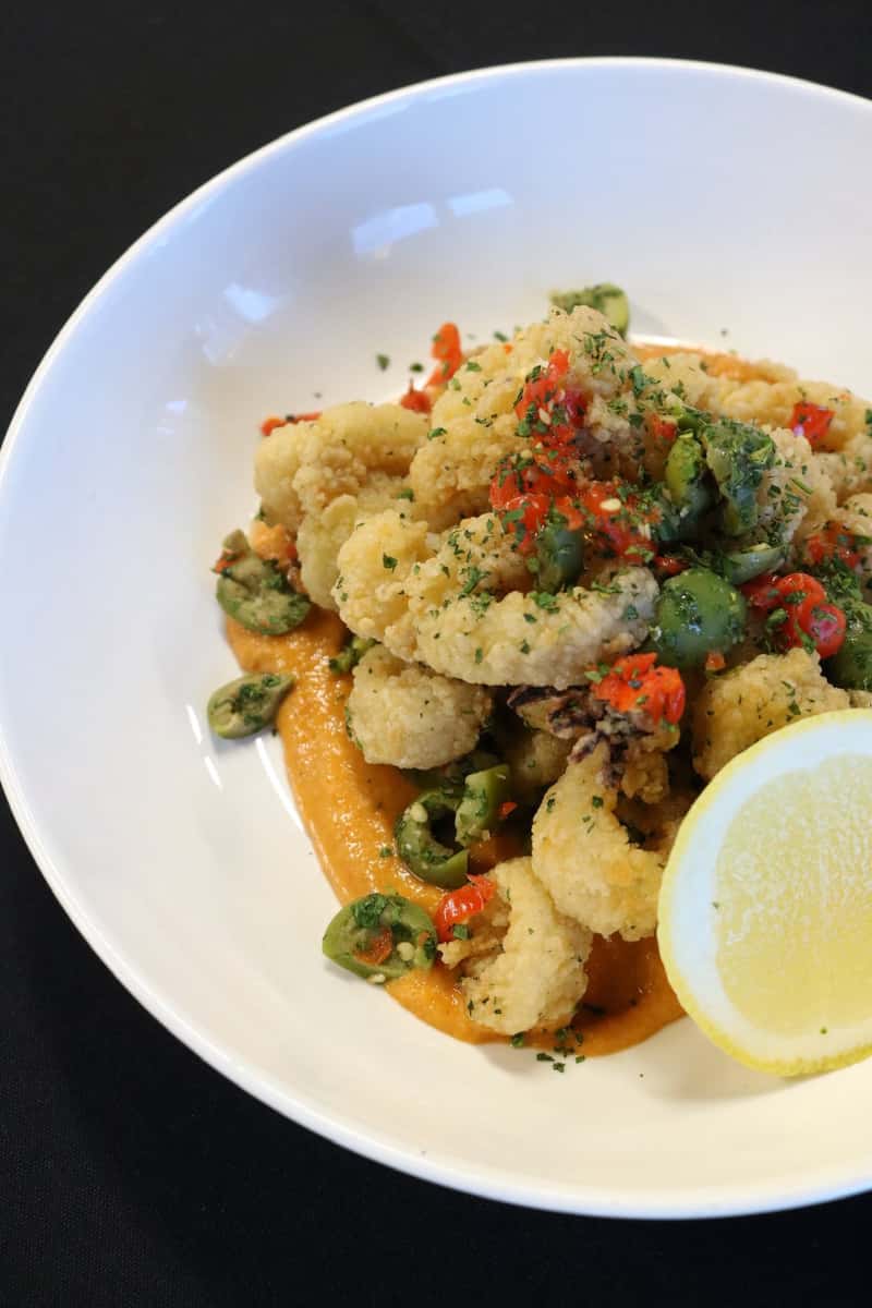 Crispy fried calamari with sliced jalapeños and red peppers served over creamy sauce with lemon wedge