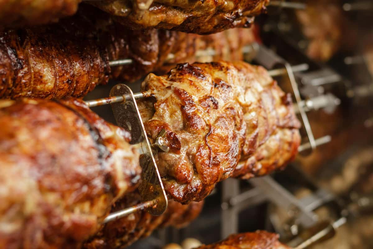 Juicy, golden-brown meat turning on a rotisserie spit inside a commercial grill.