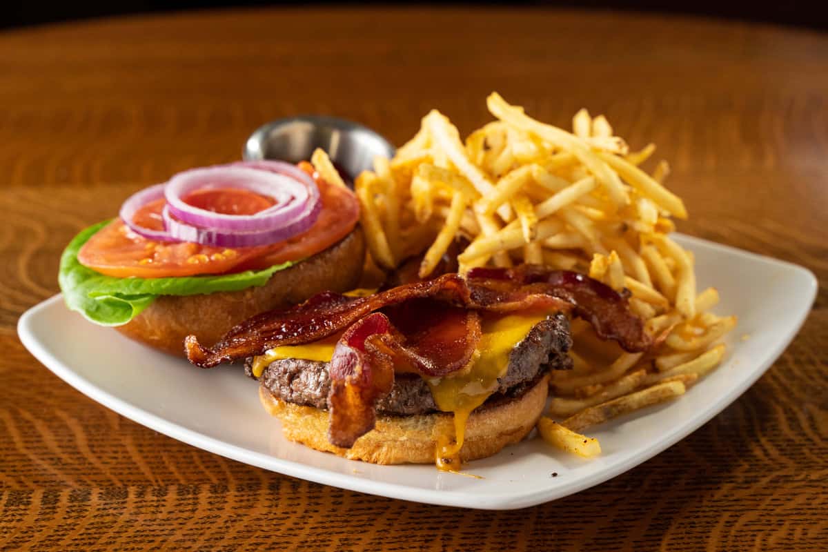 A photo of an open-faced burger with bacon and cheddar cheese, served with french fries.