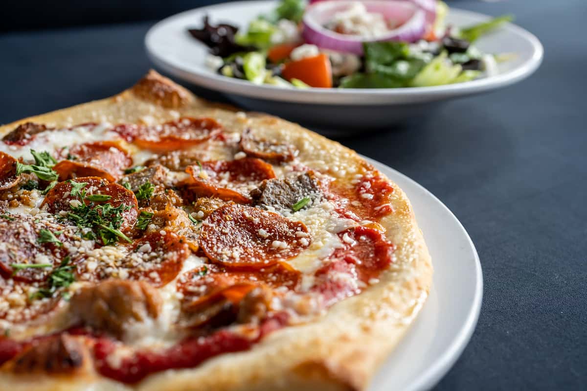 Close up pizza and salad meal combination on a dark grey table with soft lighting