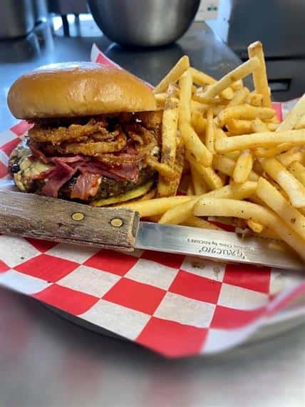 knife in front of a burger with crispy onions, bacon and cheese with a side of fries in a basket