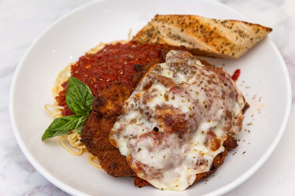 chicken parmesan with melted cheese and marinara sauce served over pasta with garlic bread
