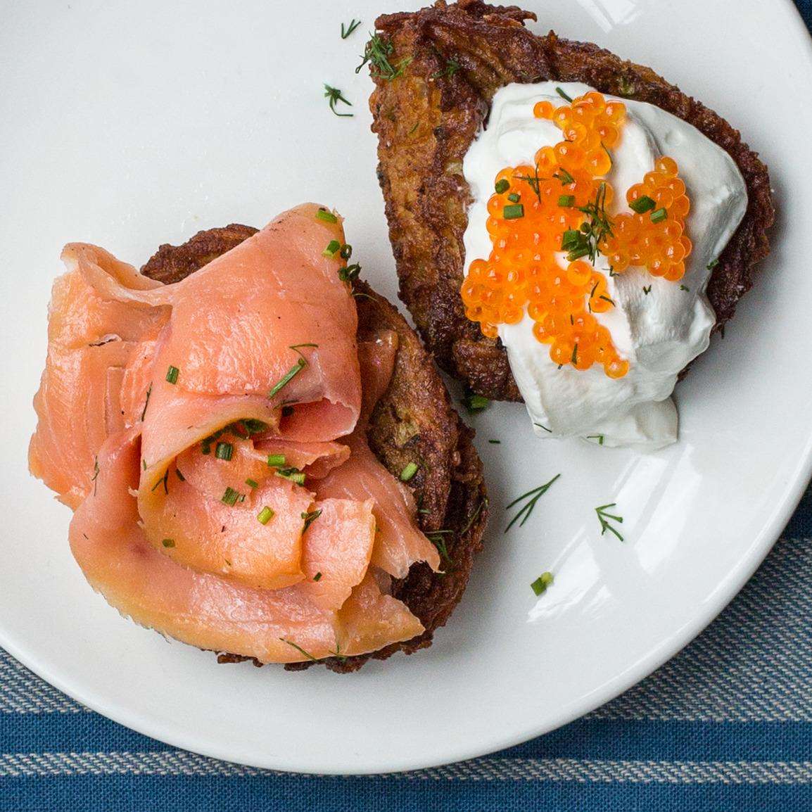 Crispy potato latkes topped with smoked salmon and sour cream with salmon roe, garnished with herbs.