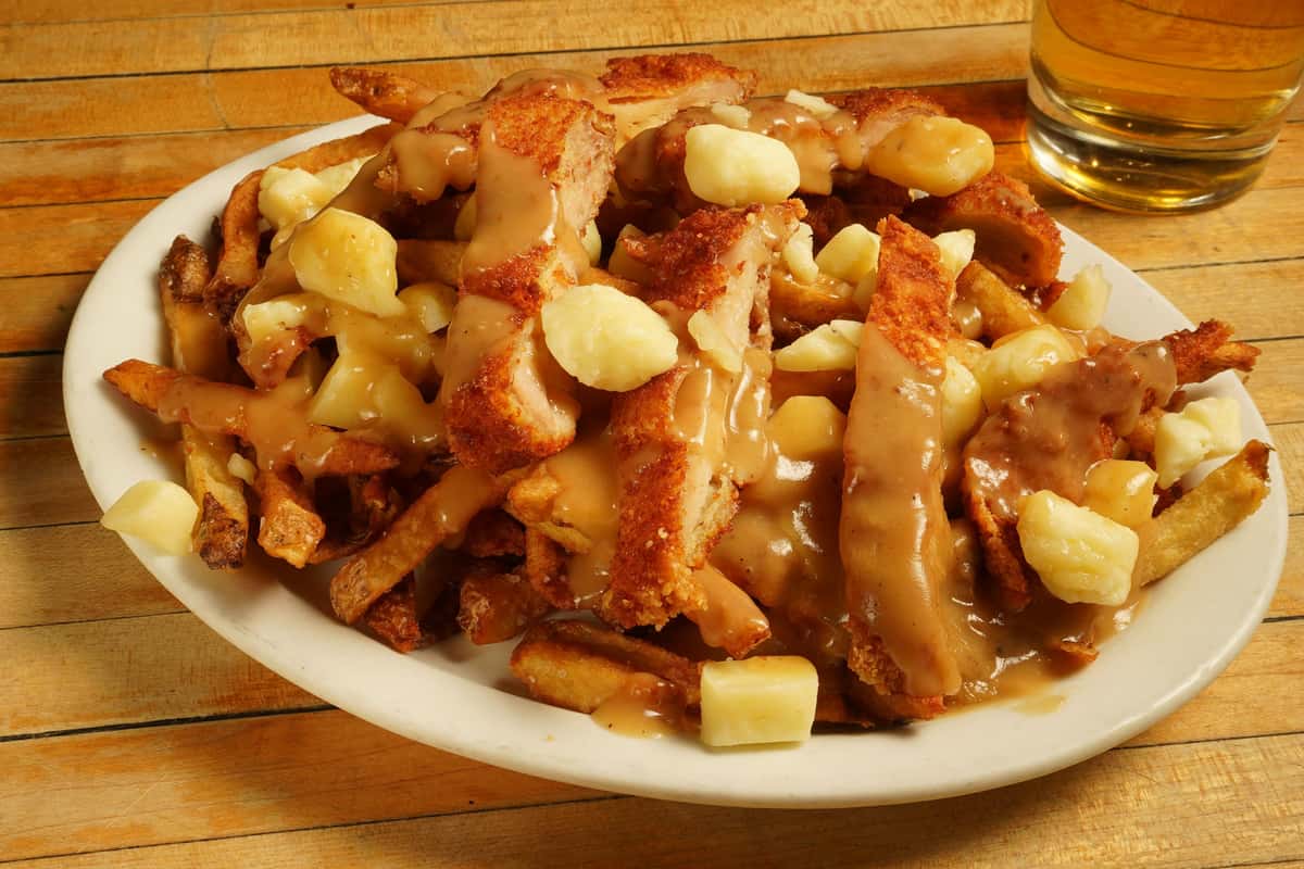 A plate of poutine, with crispy fries topped with cheese curds and smothered in rich brown gravy.