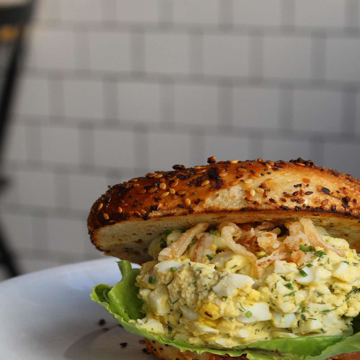 A sesame bagel sandwich filled with a generous portion of egg salad, topped with crispy onions and lettuce.