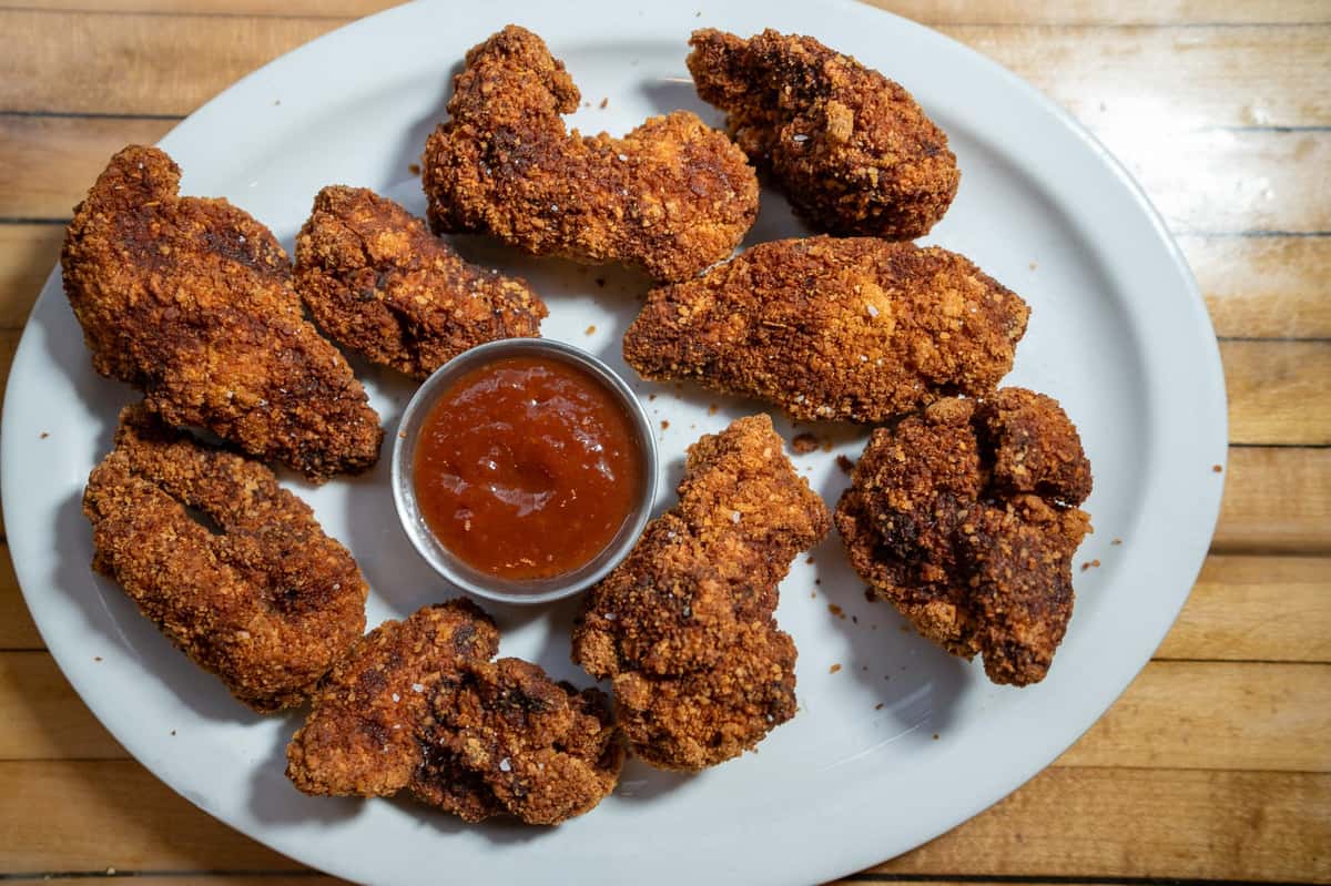 A plate of crispy fried chicken pieces with a side of dipping sauce.
