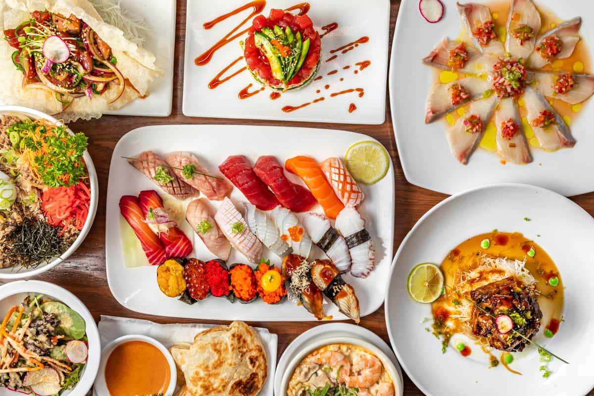A table full of a variety of Asian dishes and sushi