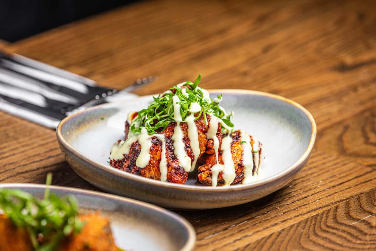 Chargrilled chicken wings drizzled with creamy white sauce, topped with fresh herbs and served in a rustic ceramic bowl.