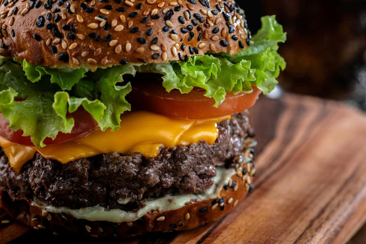 A sesame seed bun burger with beef, cheese, lettuce, and tomato sits on a wooden board at Spot Gourmet Burgers.