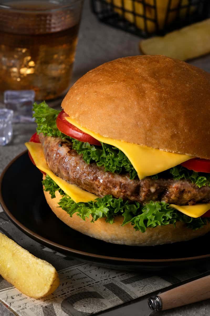 A fully loaded burger with a patty, cheese, lettuce, and tomato on a black plate, served at Spot Gourmet Burgers.