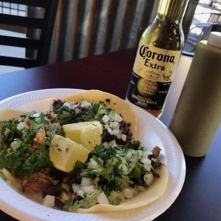 Three chicken street tacos with cilantro, onions and lime on a plate with a bottle of beer