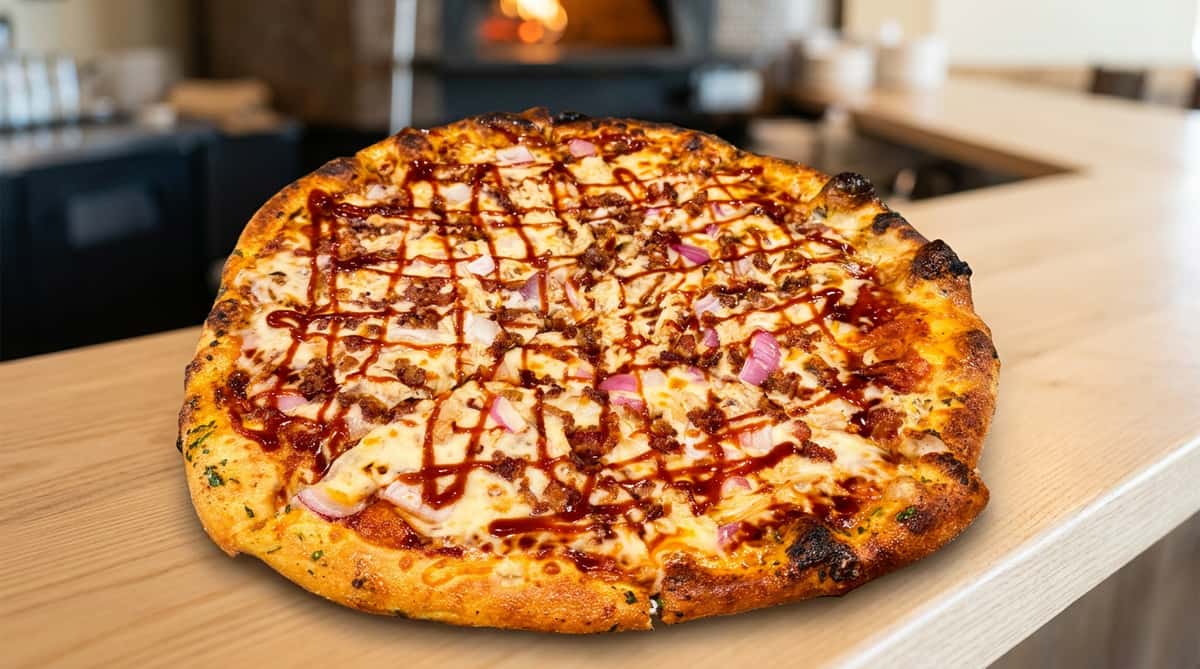 BBQ chicken pizza with melted cheese, red onions, bacon, and a balsamic glaze drizzle.