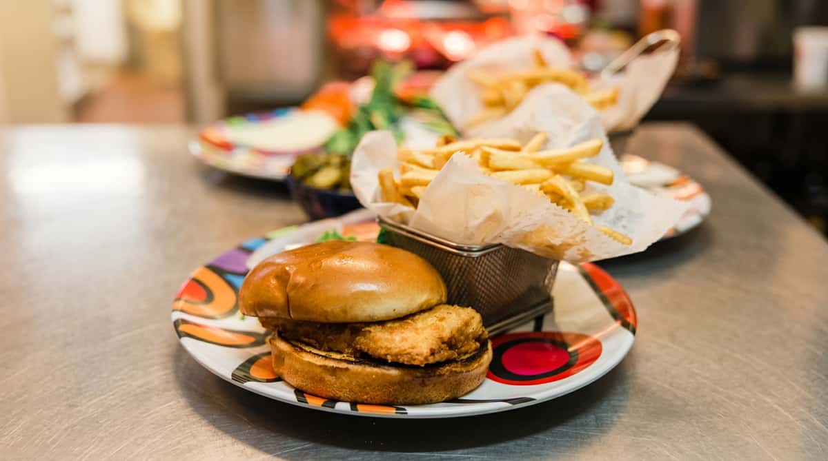 Fried fish sandwich on a bun with french fries in a metal basket.