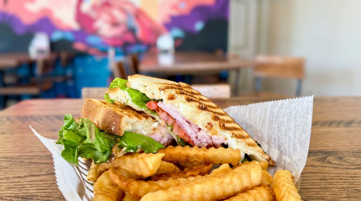Grilled panini sandwich with ham, melted cheese, lettuce, and tomato, served with crinkle-cut fries.