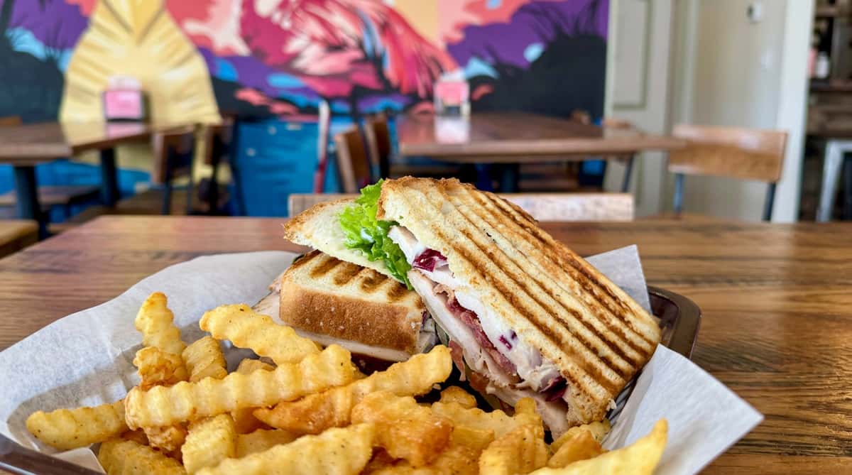 Grilled panini sandwich with turkey, bacon, red onion, and lettuce, served with crinkle-cut fries.