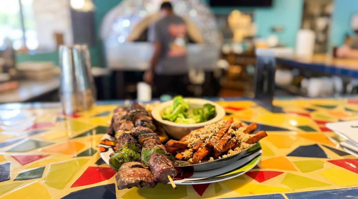 Skewers of meat and green bell peppers, sweet potato fries with topping, and a side of broccoli.