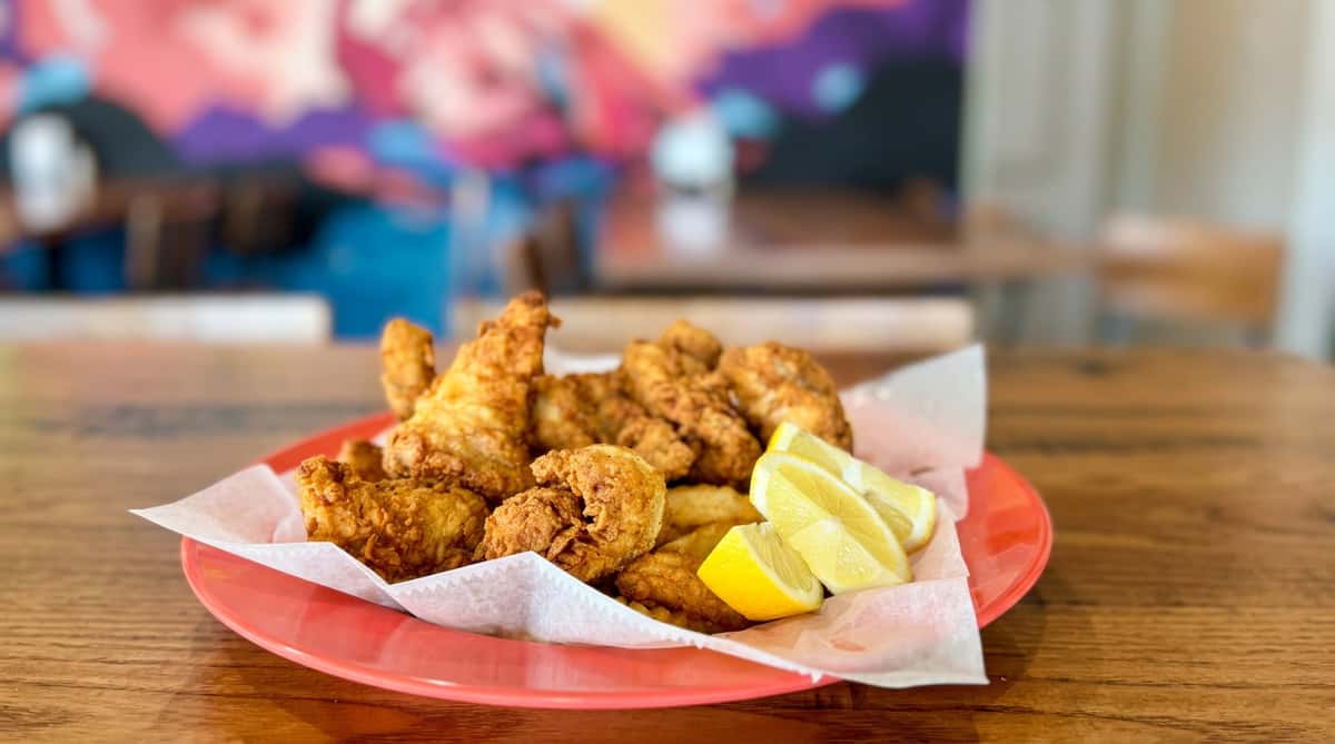 Fried fish and chips with several lemon wedges on a coral-colored plate lined with paper.
