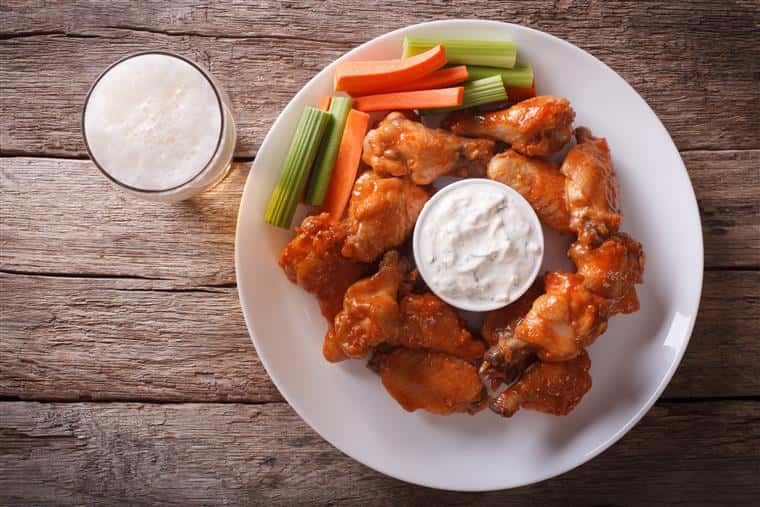 Plate of buffalo wings with side of celery, carrots, bleu cheese.  Full beer glass to side.