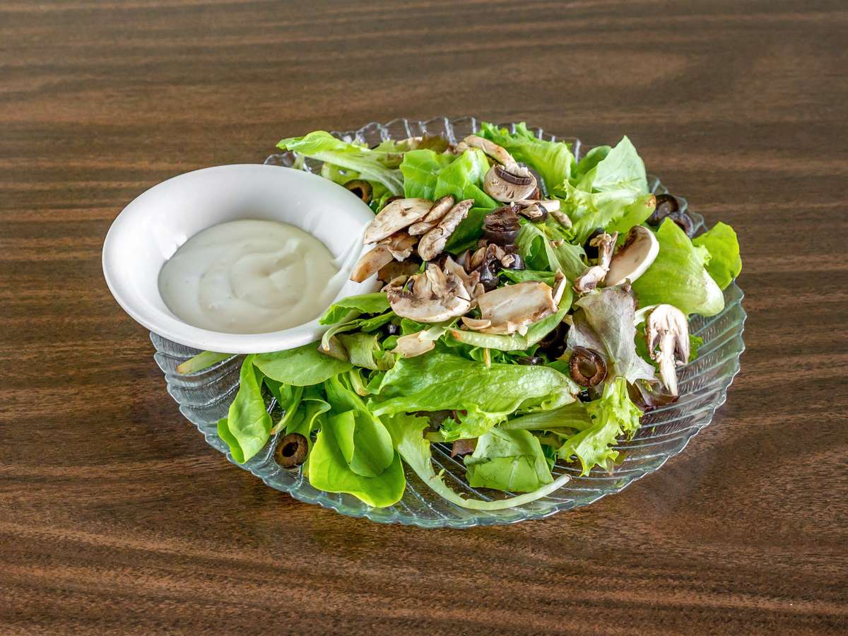 Miller's Cafe fresh green salad with sliced mushrooms, olives, and a side of creamy white dressing on a dark wood table.