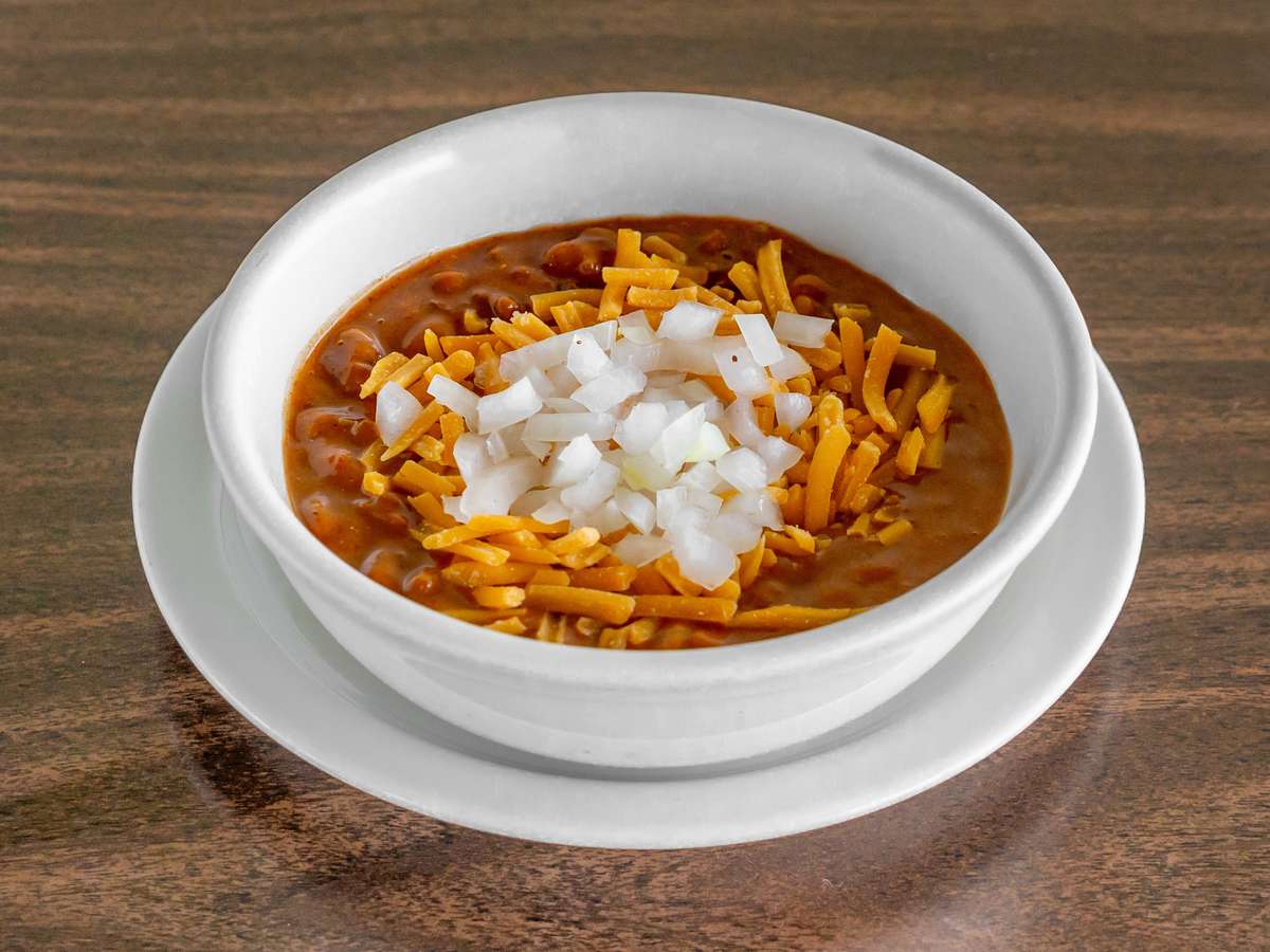 Miller's Cafe hearty chili bowl topped with shredded cheddar cheese and diced white onions on a dark wood table.