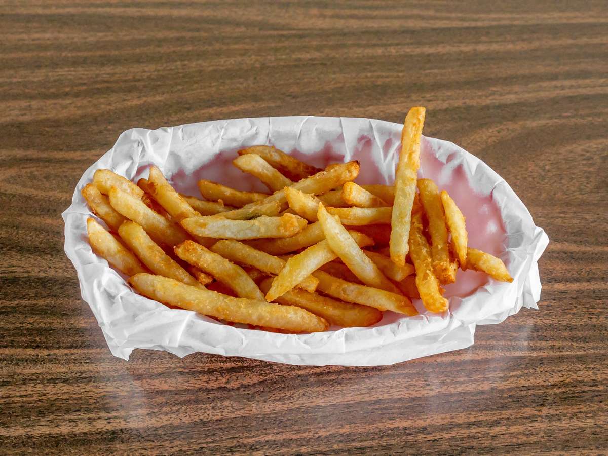 Golden french fries in a white paper basket on a wood table from Miller's Cafe.