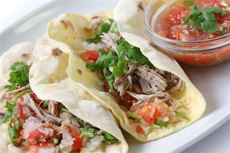 Two meat tacos topped with chopped parsley, diced tomato and onions, served with a side of salsa 