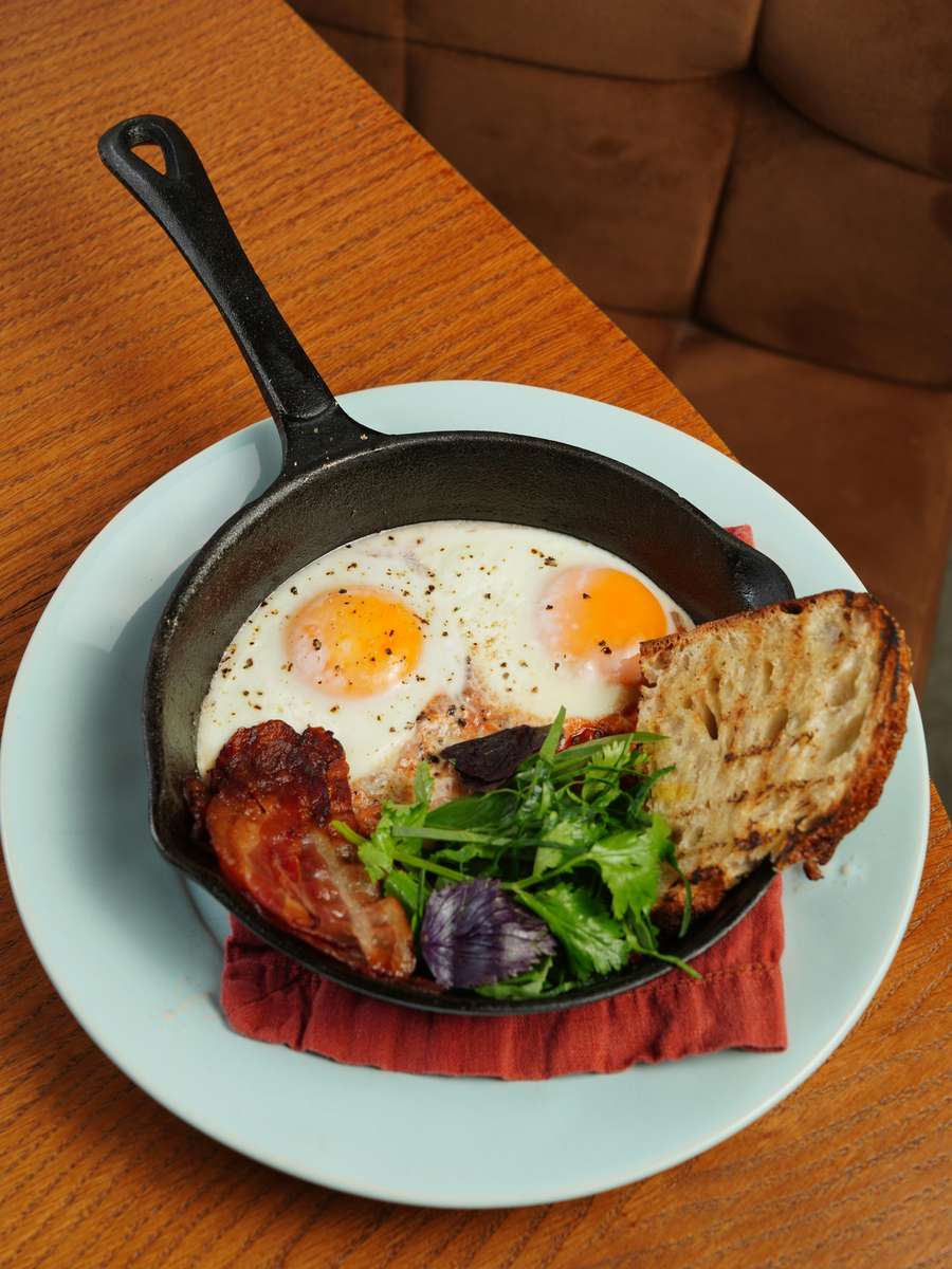 A Tennessee Grill cast iron skillet holds two fried eggs, bacon, greens, and toast.