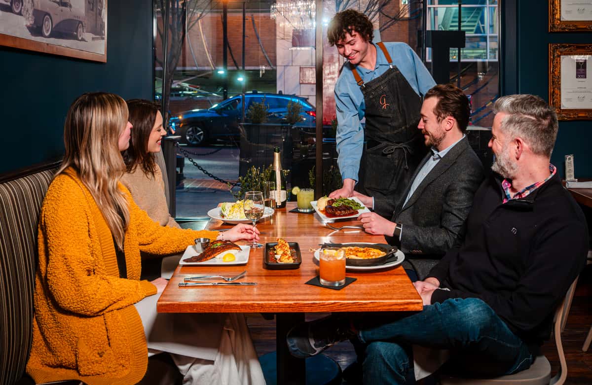 Smiling waiter bringing food to a table of four