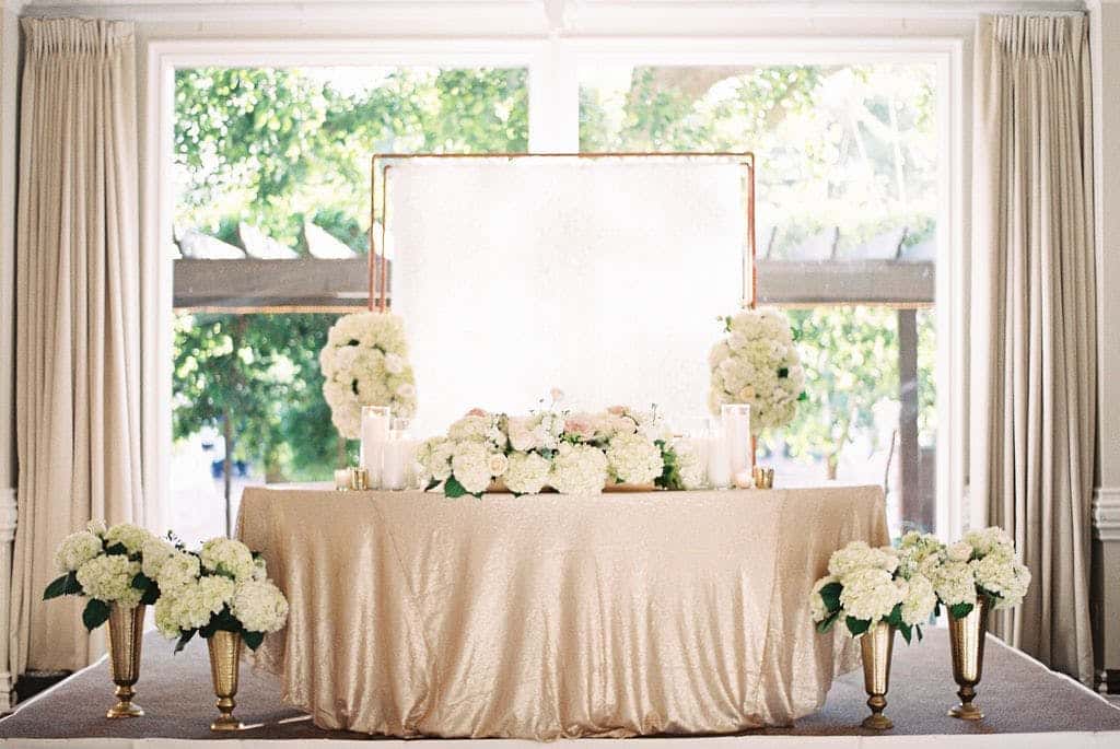 Gift table decorated in white flowers with gold vases and candles