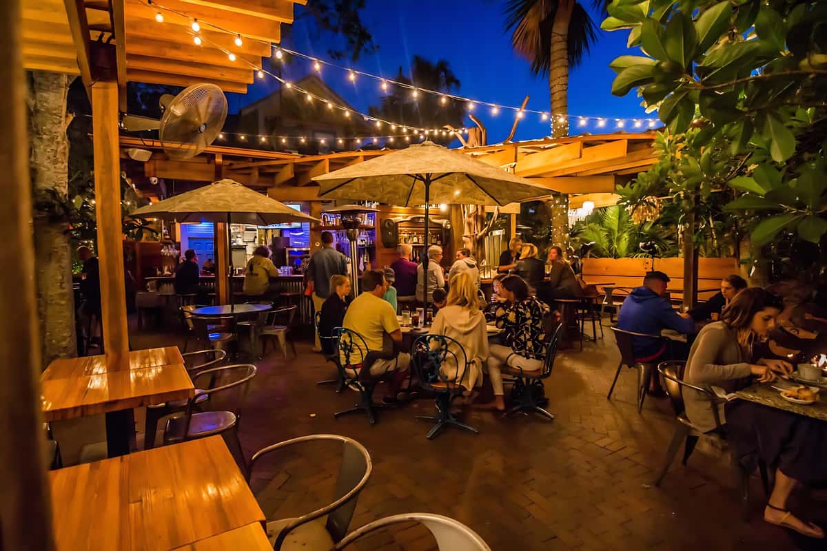 Evening dining on the patio with guests gathered around tables beneath café lights and tropical greenery.