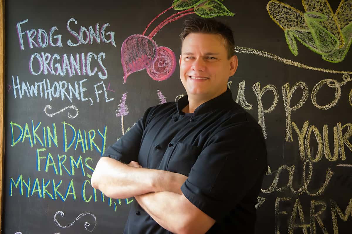 Chef David Hauser standing before a chalkboard highlighting local farms and fresh ingredients featured in our seasonal menu.