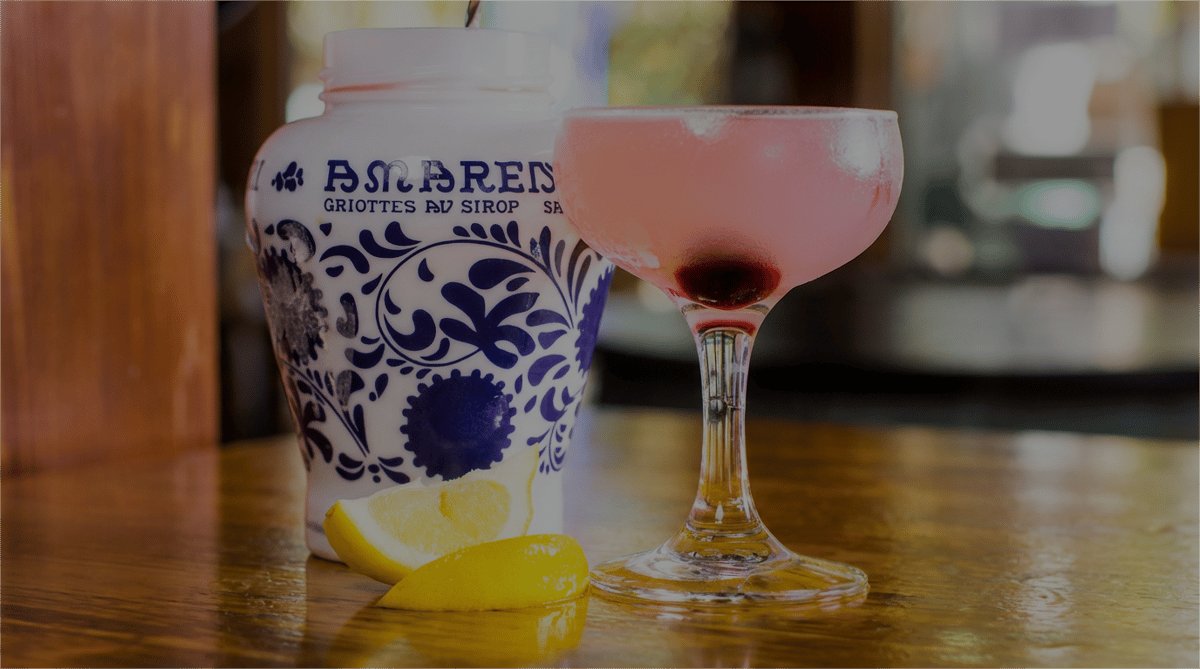 A chilled pink cocktail served in a coupe glass with cherry garnish, offering a bright and refreshing flavor profile.