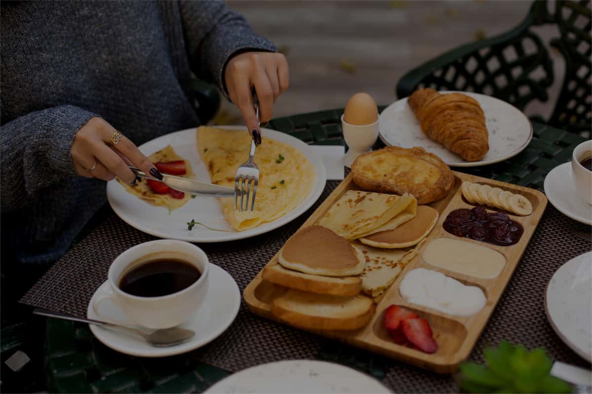 A fresh brunch spread featuring a fluffy omelet, delicate crepes, pancakes, pastries, fresh fruit, and coffee, served on an outdoor café table for a relaxed morning dining experience.