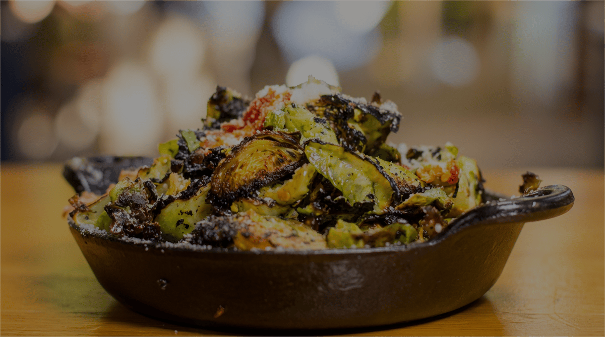 Crispy roasted Brussels sprouts finished with parmesan and house seasoning, served in a cast-iron skillet for a bold and savory small plate.