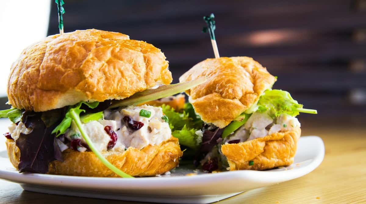 House-made chicken salad served on a flaky croissant with mixed greens and cranberries, offering a fresh and satisfying lunch option.