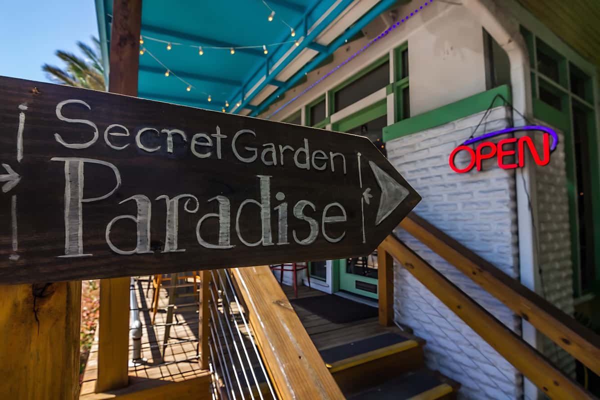 Handcrafted wooden sign pointing toward the Secret Garden Paradise patio dining area.