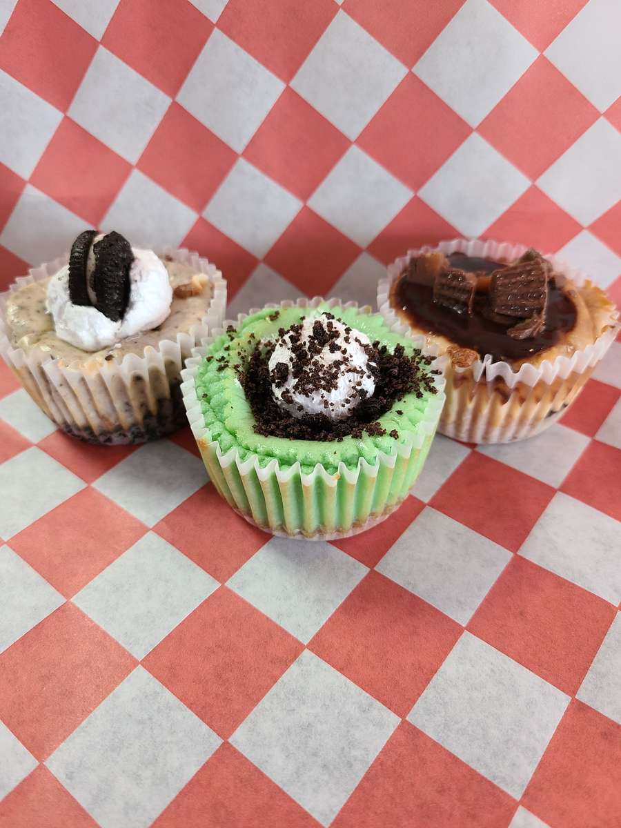 Three vibrant mini cheesecakes with diverse toppings on a red and white checkered background.
