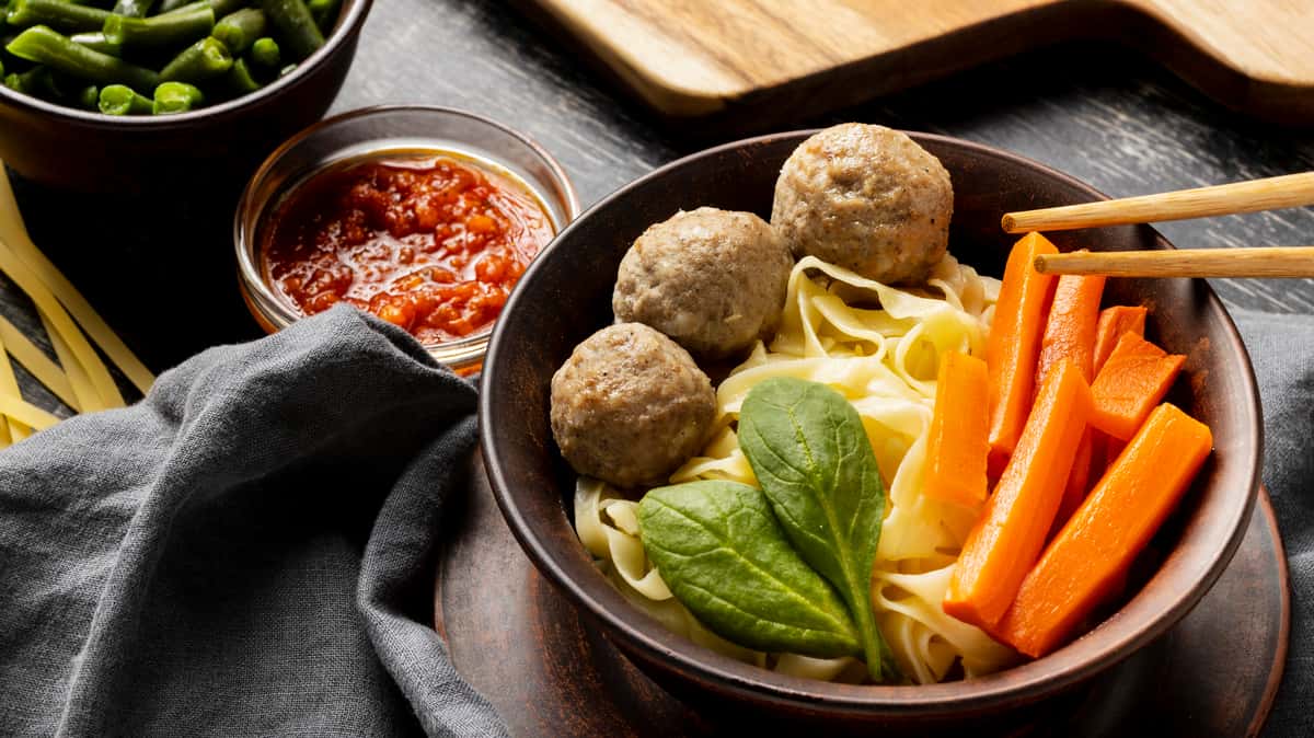 meatballs, spinach, carrots on fat noodles with dips on the side