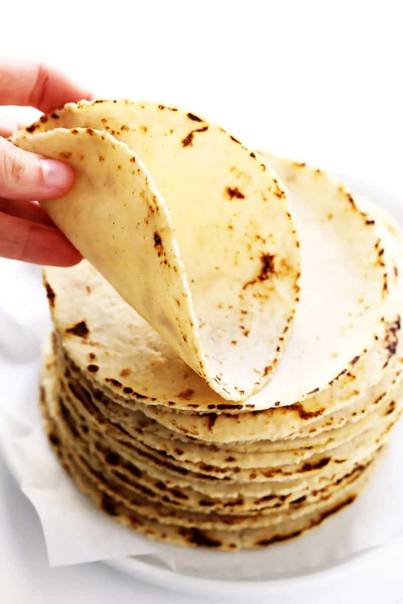 Hand lifting a freshly made corn tortilla from a stack on a white plate